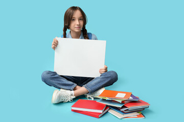 Schoolgirl with blank poster and stationery sitting on color background