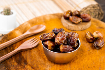Delicious dry dates, popular fruit dates during the month of Ramadan on a round wooden board with wooden spoon and fork