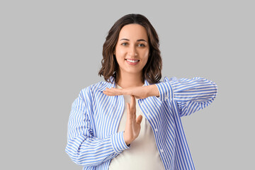 Young woman showing time-out gesture on light background. Rules concept