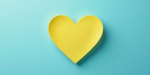 A vibrant yellow heart shape crafted from felt material, delicately positioned against a serene light blue backdrop, offers a simple yet captivating visual representation of affection and warmth.