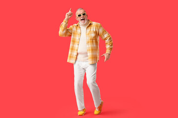 Happy senior man in sunglasses dancing on red background. National Grandpa Day
