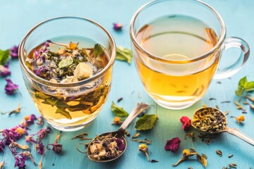 Herbal tea in glass cups with dried flowers and mint leaves on blue wooden background.