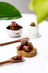 Portrait image of delicious sweet dates, sweet dried dates fruit popular during Ramadan, typical fruit of fasting month. served on white table with ornamental plants, wooden spoon and fork