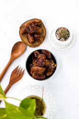 Portrait image of delicious sweet dates, sweet dried dates fruit popular during Ramadan, typical fruit of fasting month. served on white table with ornamental plants, wooden spoon and fork