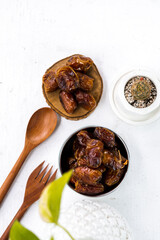 Portrait image of delicious sweet dates, sweet dried dates fruit popular during Ramadan, typical fruit of fasting month. served on white table with ornamental plants, wooden spoon and fork