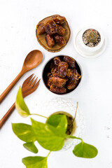 Portrait image of delicious sweet dates, sweet dried dates fruit popular during Ramadan, typical fruit of fasting month. served on white table with ornamental plants, wooden spoon and fork