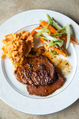 Sliced brisket with sweet potato puree and braised vegetables filling a dinner plate
