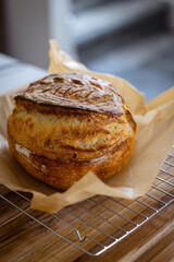 fresh loaf of traditional sourdough bread resting on parchment paper and a wire cooking rack