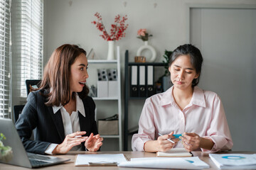 Two women engaged in a business discussion at a modern office table with documents and a laptop.