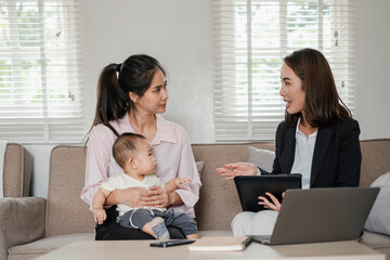 Businesswoman consulting a mother holding her baby in a modern living room, highlighting...