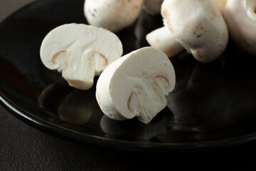 A view of white button mushrooms on a plate, feature one halved mushroom.