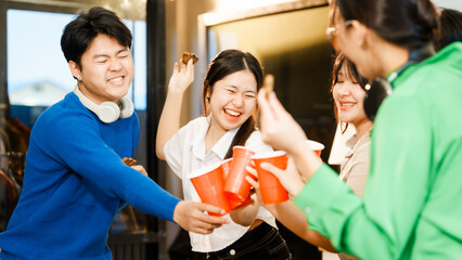 A group of young Asian teenage friends are having a college party at home. They eat food and drink, talk, laugh, and share a good time together in a fun and lively atmosphere