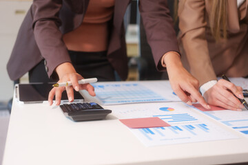 Fototapeta premium Close-up of two businesswomen working at desk discussing business strategies, analyzing financial charts, planning marketing plans and using laptop to drive business growth in professional office