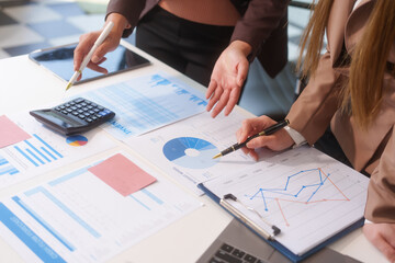 Close-up of two businesswomen working at desk discussing business strategies, analyzing financial charts, planning marketing plans and using laptop to drive business growth in professional office