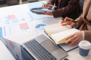 Close-up of two businesswomen working at desk discussing business strategies, analyzing financial charts, planning marketing plans and using laptop to drive business growth in professional office
