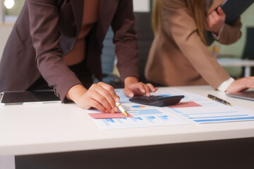 Close-up of two businesswomen working at desk discussing business strategies, analyzing financial charts, planning marketing plans and using laptop to drive business growth in professional office