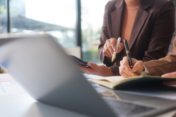 Close-up of two businesswomen working at desk discussing business strategies, analyzing financial charts, planning marketing plans and using laptop to drive business growth in professional office