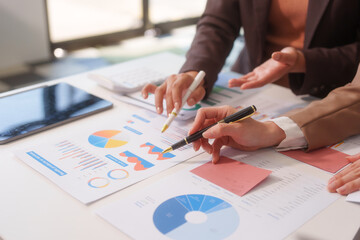 Close-up of two businesswomen working at desk discussing business strategies, analyzing financial charts, planning marketing plans and using laptop to drive business growth in professional office