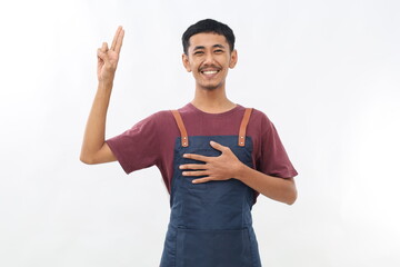 Asian young man wearing apron over white background smiling swearing with hand on chest and fingers...