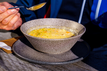 Man spooning barley soup in mountain inn. Wooden table, rustic ambience, open air