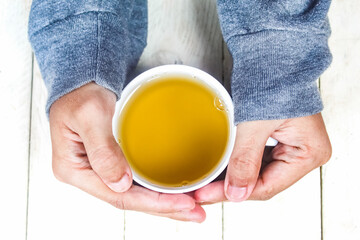 both hands holding a cup of tea on the wooden table