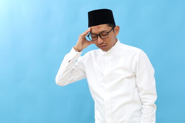 Unhealthy Asian Muslim man suffering from headache or migraine isolated on blue background