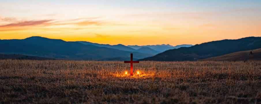 A scenic sunset view featuring a glowing cross in an open field, surrounded by mountains, creating a serene and spiritual atmosphere.