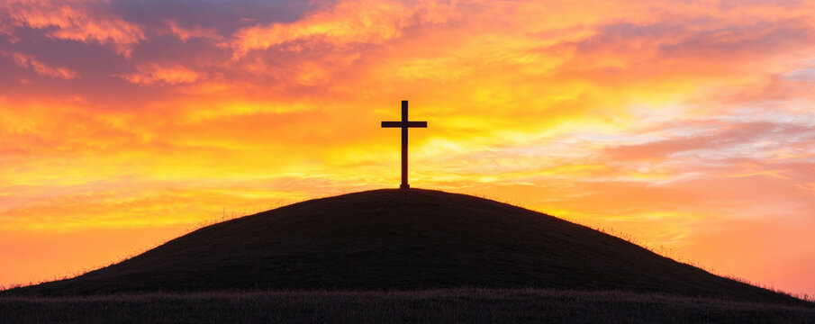 A silhouette of a cross atop a hill with a vibrant sunset in the background, symbolizing faith and spirituality.