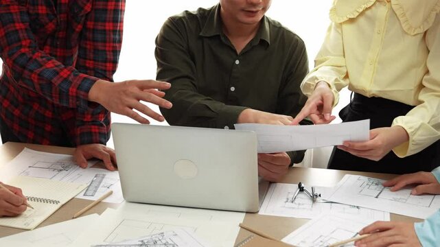Smart architect and safety engineer discussion about building plan on table with architectural document, measurement tools and wooden block scatter around at modern office. Closeup. Delineation.