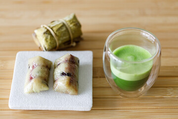Cup of fresh matcha tea, green tea and Coconut steamed sticky rice with banana, Thailand dessert on wooden table.