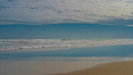 Low tide in the ocean. The waves roll towards the shore, foam and spread over the sandy beach. Blue sky, white clouds. Reflection on wet, smooth sand. Madagascar. Morondava.  The vast expanse.