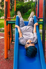 Obraz premium Photo of a Colombian Latino mestizo pre-teen with blue hair lying on a slide with his head down