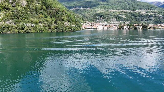4k drone footage of emerald waters of Lake Como, with the town of Dongo in the distance in Italy
