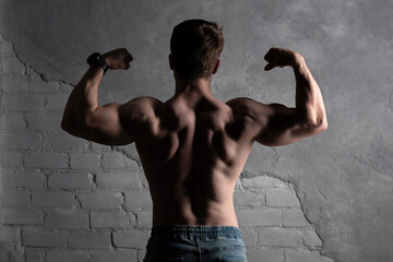 Shirtless man flexing biceps, defined muscles against textured wall.