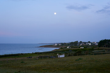 Landscape at dusk over village near the coast by the sea. Full moon in the night sky. France, Brittany.