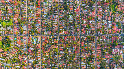 Aerial view of residential neighborhood with streets and rooftops; lush green areas visible in background. Potential use for real estate, travel, and urban planning