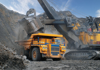Industrial excavator loading ore into big yellow truck of quarry. Open-pit mining of coal, ore, granite. No AI tools