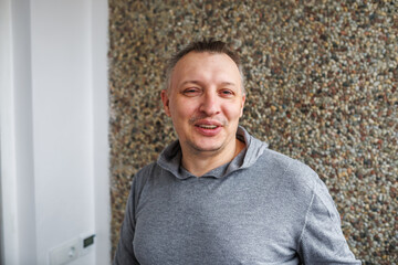 Portrait of a cheerful middle-aged smiling man wearing a gray hoodie, standing against a textured...