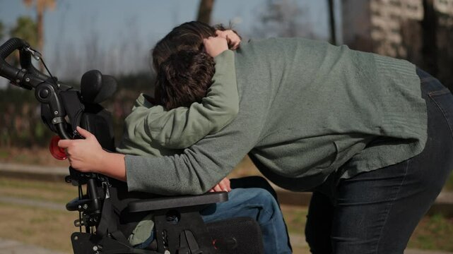 Mother hugging disabled son in wheelchair at park