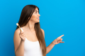 Obraz premium Young caucasian woman brushing teeth isolated on blue background pointing back