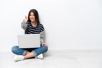Young caucasian woman with a laptop sitting on the floor isolated on white background shaking hands...