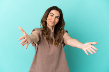 Fototapeta premium Middle aged caucasian woman isolated on blue background presenting and inviting to come with hand