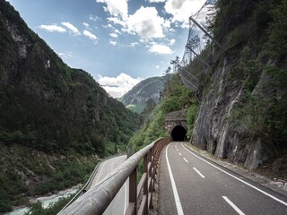 A winding cycling path on the Alpe Adria route leads into a stone tunnel, surrounded by steep rocky...