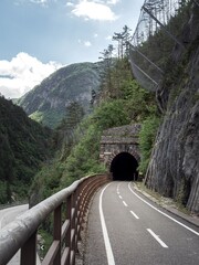 A winding cycling path on the Alpe Adria route leads into a stone tunnel, surrounded by steep rocky...
