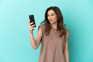 Fototapeta premium Middle aged caucasian woman isolated on blue background making a selfie