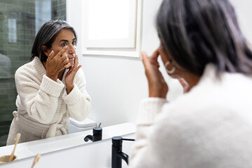 Mature woman looking eye in bathroom mirror. Putting contact lenses.