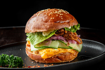 Delicious gourmet burger featuring a toasted sesame bun, fresh lettuce, creamy mayonnaise, crispy fried onions, cheese, and cucumber slices, served on a sleek black plate.