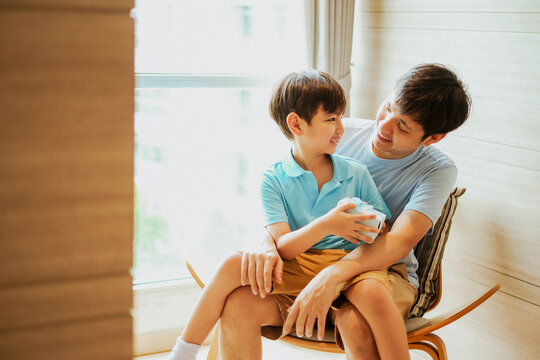 Asian boy give a gift box to his father, Dad and son embrass each other with love and happiness, Relationship in family concept. Celebrate for father day and birthday in living room.