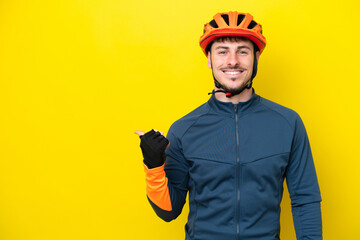Young cyclist caucasian man isolated on yellow background pointing to the side to present a product