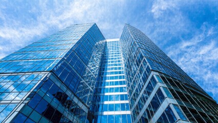 Obraz premium A modern skyscraper with reflective glass windows, reaching towards a blue sky with scattered clouds. The building's sleek design and mirrored surfaces create a striking visual effect